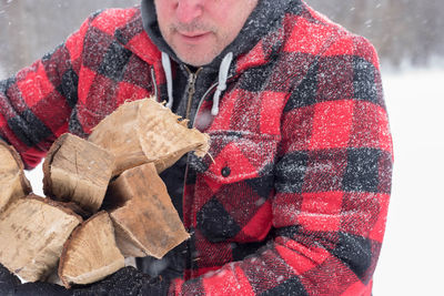 Midsection of mature man with wood standing outdoors during snow fall