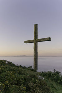 Commemorative wooden cross on a hill above lowland fog in dawn light