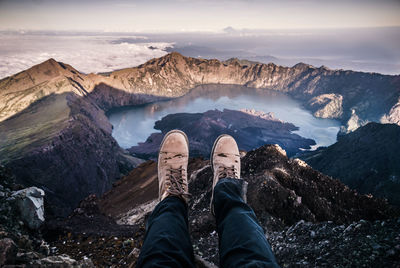 Low section of person relaxing on mountain by lake