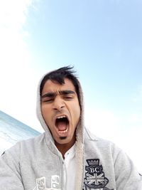 Low angle view portrait of young man yawning against sky