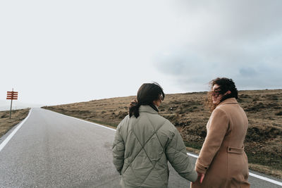 Rear view of people walking on road against sky