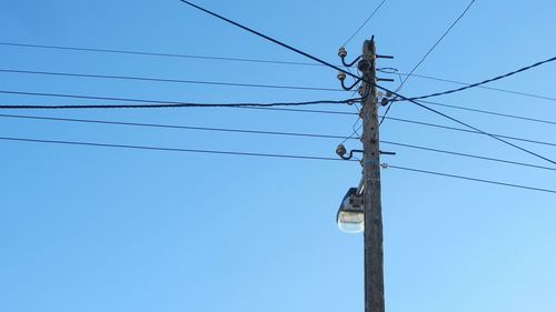 Low angle view of electricity pylons and street light against clear blue sky