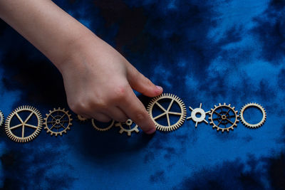 Cropped hand of person holding cogwheel over colored background