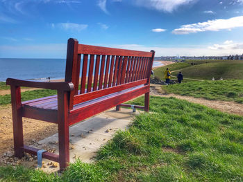 Empty bench on field against sky