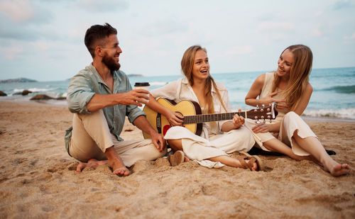 Friends sitting at beach against sky