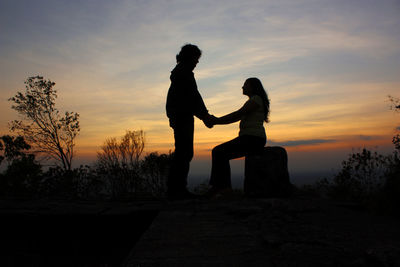 Silhouette couple standing against orange sky during sunset