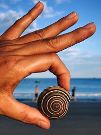 Close-up of person holding shell against sea