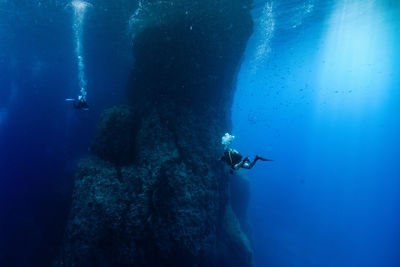 Men scuba diving by rock formation in sea at gozo