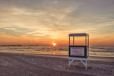 Information sign on beach against sky during sunset