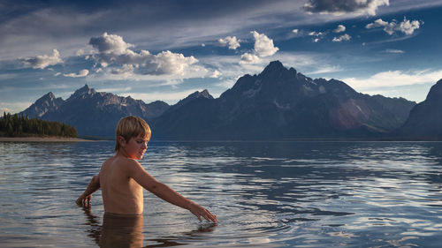Shirtless man in lake against mountains and sky