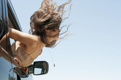 Woman bending from car window against clear sky