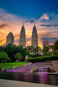 Buildings by river against sky during sunset