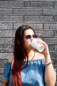 Young woman drinking water against wall