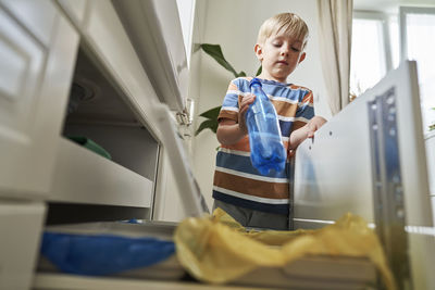 Blond boy throwing plastic bottle in garbage bin