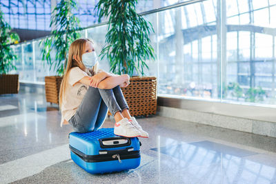 Full length of girl wearing mask sitting at airport