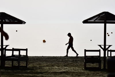 Silhouette people playing soccer on beach against clear sky