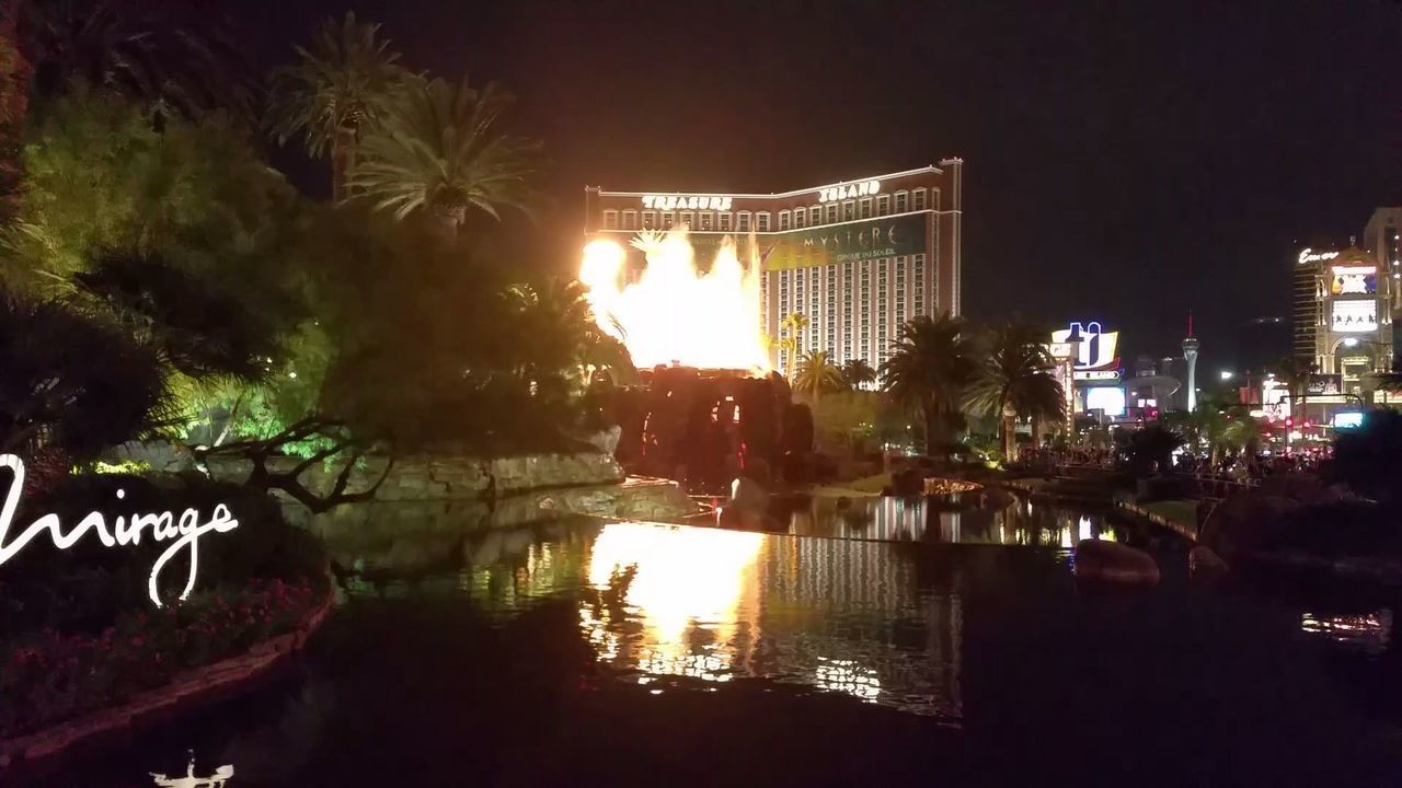 ILLUMINATED BUILDINGS BY LAKE AT NIGHT