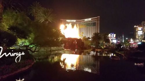 Illuminated buildings by lake against sky in city at night