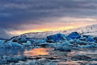 Frozen sea against dramatic sky during sunset