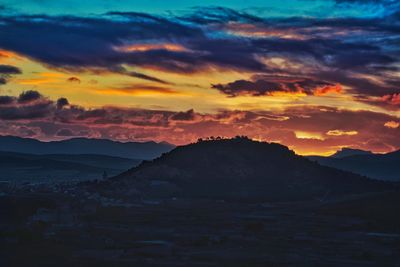 Scenic view of silhouette mountains against dramatic sky during sunset