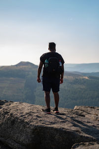 Rear view of backpacker standing on rock against sky