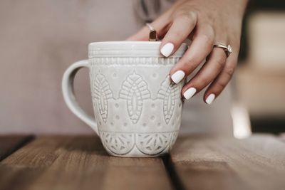 Close-up of woman holding coffee cup on table
