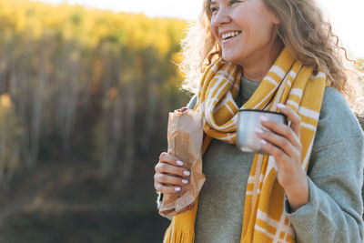 Young happy beautiful woman traveller with curly hair eating hot dog and drinking tea 