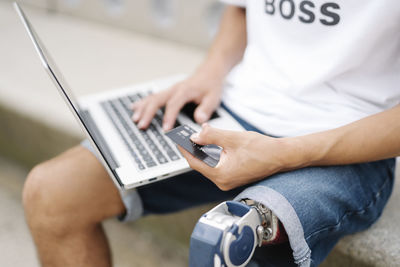 Man holding credit card while working on laptop outdoors