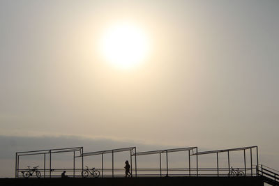 Silhouette woman standing by railing against sky during sunset