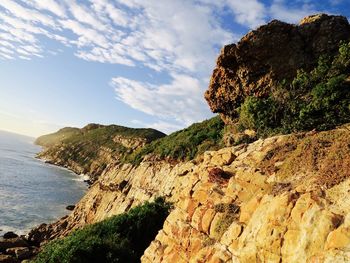 Tilt shot of cliff by sea against sky