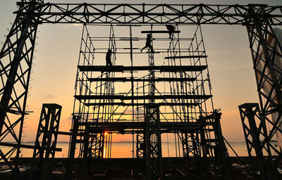Low angle view of workers on silhouette scaffolding against sky during sunset