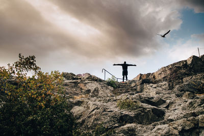 Low angle view of male athlete standing with arms outstretched on hill against sky