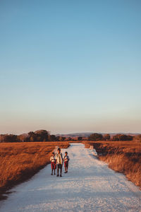 Rear view of people walking on snowy field against clear sky during winter