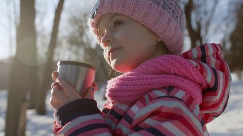 Cute girl holding drink while standing outdoors during winter