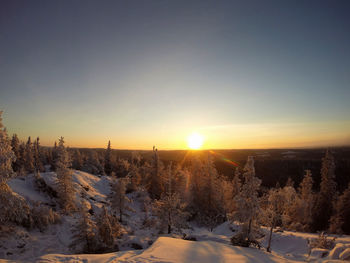 Snow covered field against sky during sunset