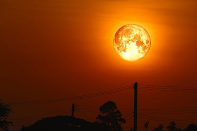 Low angle view of silhouette electricity pylon against orange sky