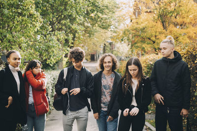 Male and female friends standing on footpath amidst trees in park