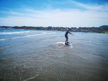 Full length of boy balancing while surfing in sea against sky