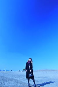 Rear view of woman standing on beach against clear blue sky