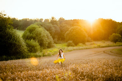 A girl runs through a field with spikelets against the background of the setting sun