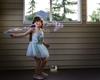 Full length of girl playing with bubbles by window