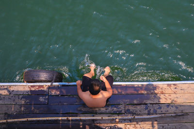 High angle view of shirtless boy sitting on boat deck over lake