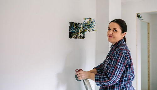 Young woman looking away while standing against white wall