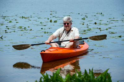 Senior male enjoys keeping active in an orange kayak on a small pond