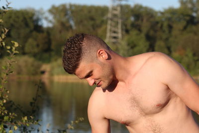 Shirtless young man standing against trees in forest