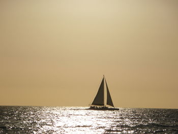 Sailboat sailing on sea against clear sky during sunset