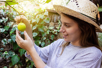 Close-up of woman wearing hat picking lemon from plant