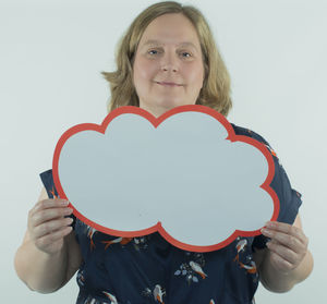 Portrait of smiling woman holding heart shape over white background