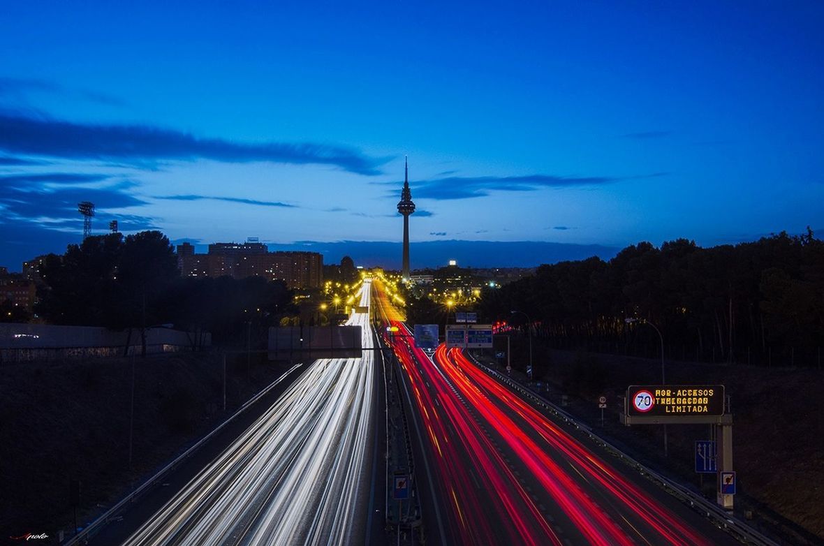 LIGHT TRAILS ON ROAD IN CITY AGAINST BLUE SKY