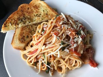 Overhead view of spaghetti with garlic bread served in white plate